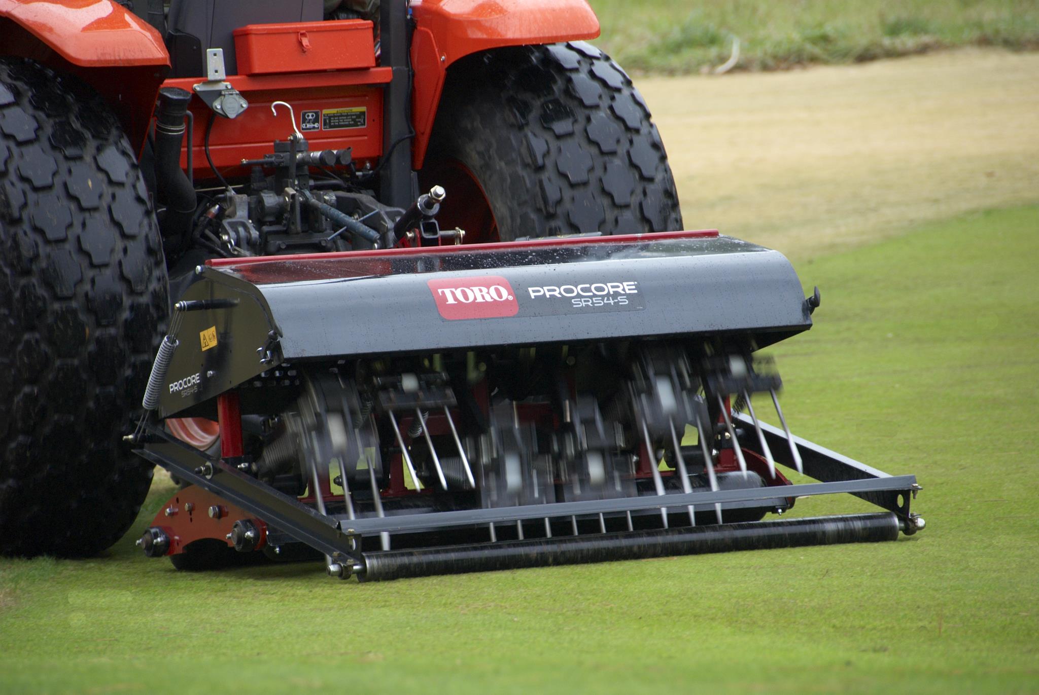 A Toro ProCore SR54s aerator being towed by a tractor on a golf course.