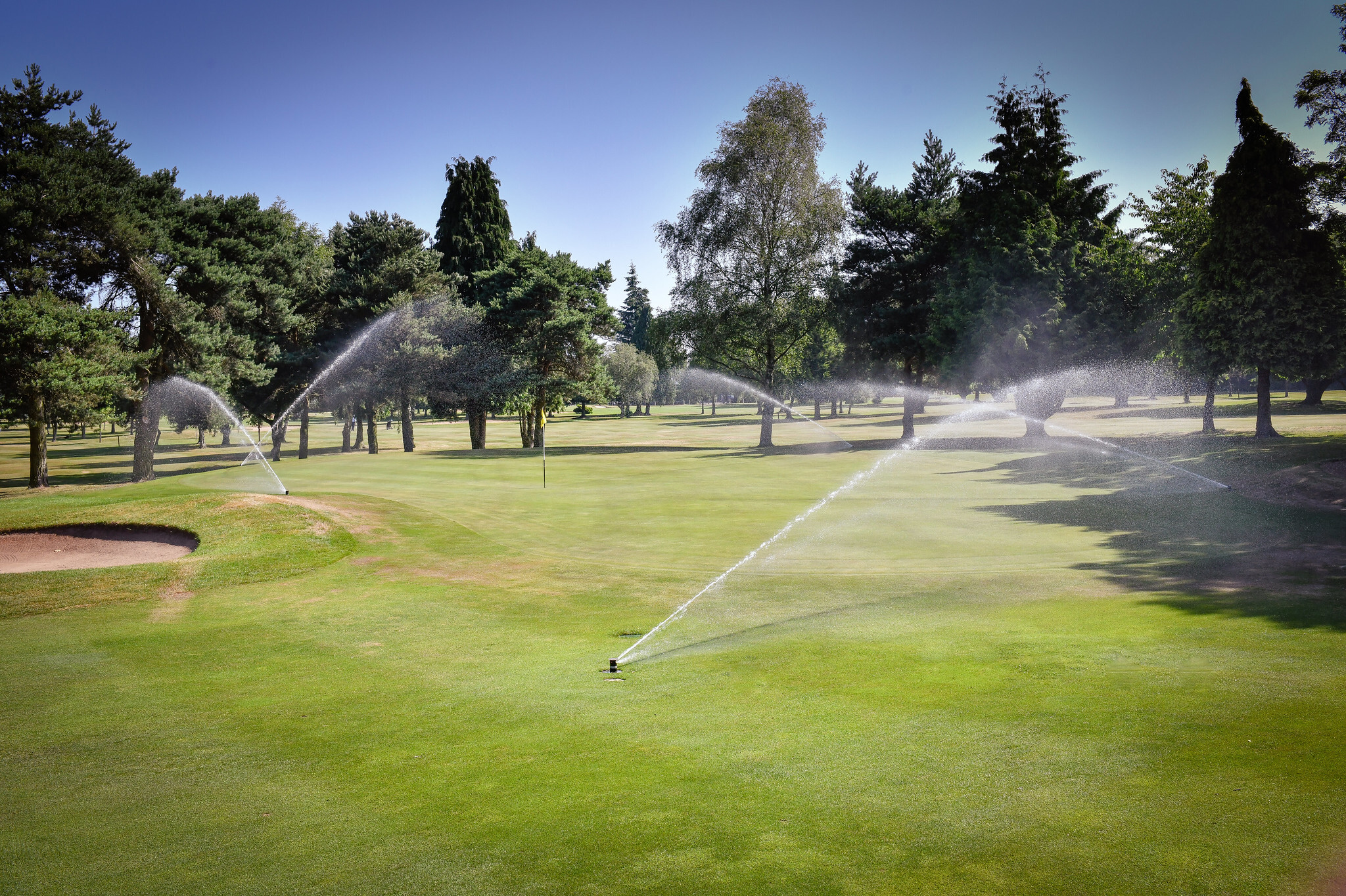 Golf course fairway with automated Toro irrigation sprinklers in operation on a sunny day, promoting efficient water management.
