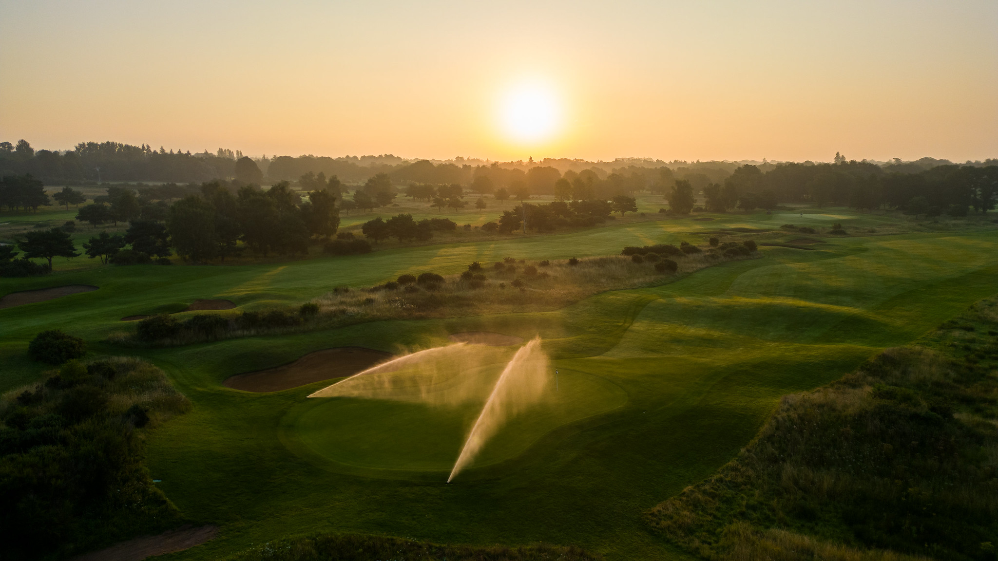 Aerial view of golf course green with Toro irrigation sprinklers running at sunrise, promoting sustainable turf management.