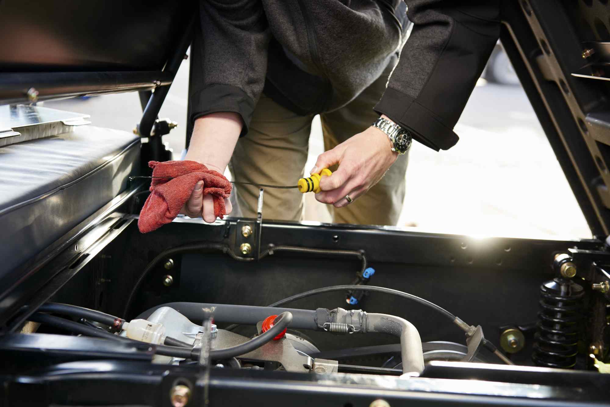 Technician performing maintenance under vehicle bonnet, checking fluid levels as part of Reesink Aftercare service.