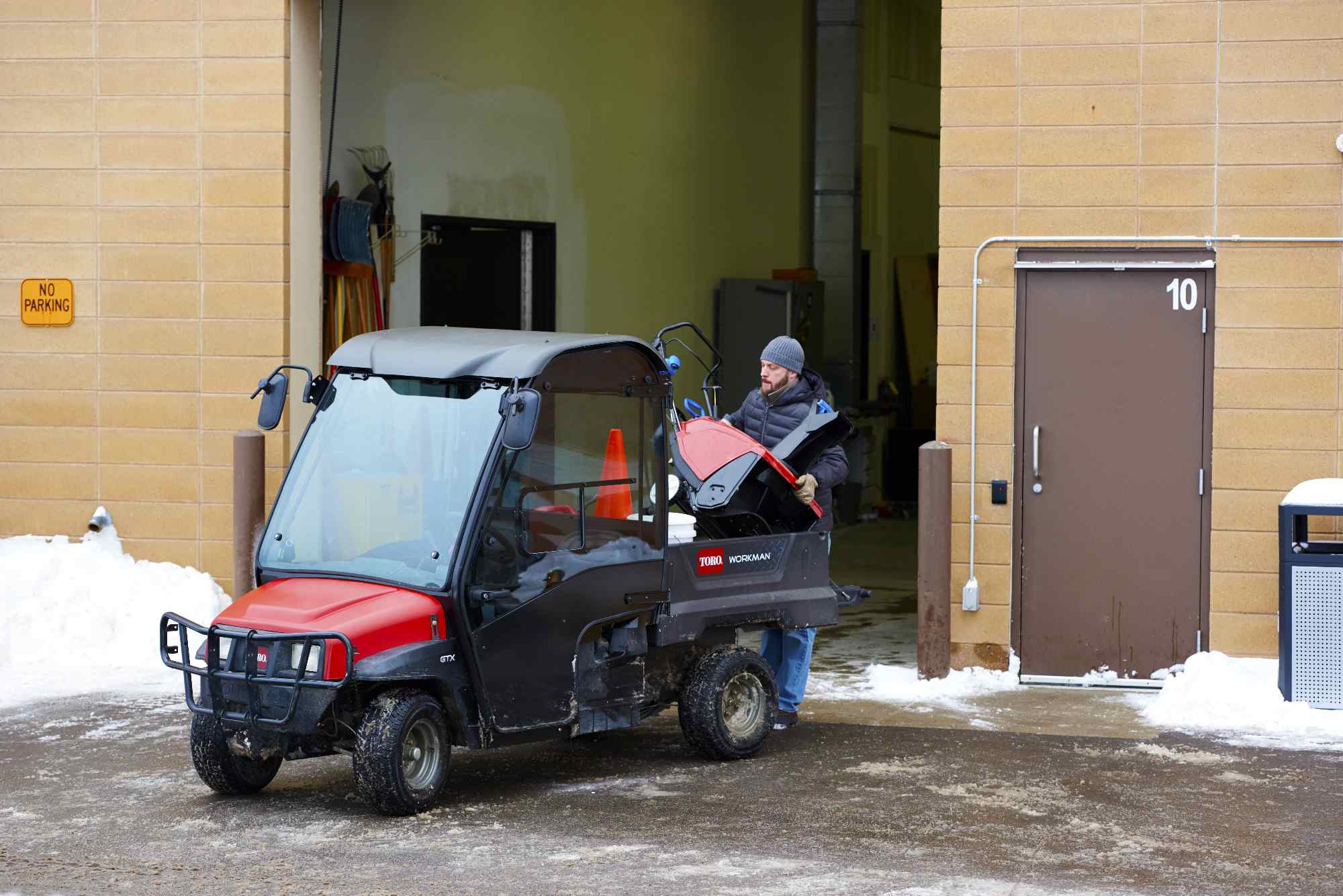 Toro Workman utility vehicle being prepared for use in snowy conditions outside maintenance workshop.