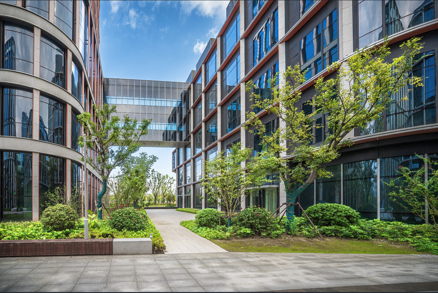 Modern sustainable office buildings with landscaped courtyard and glass bridge walkway under blue sky.