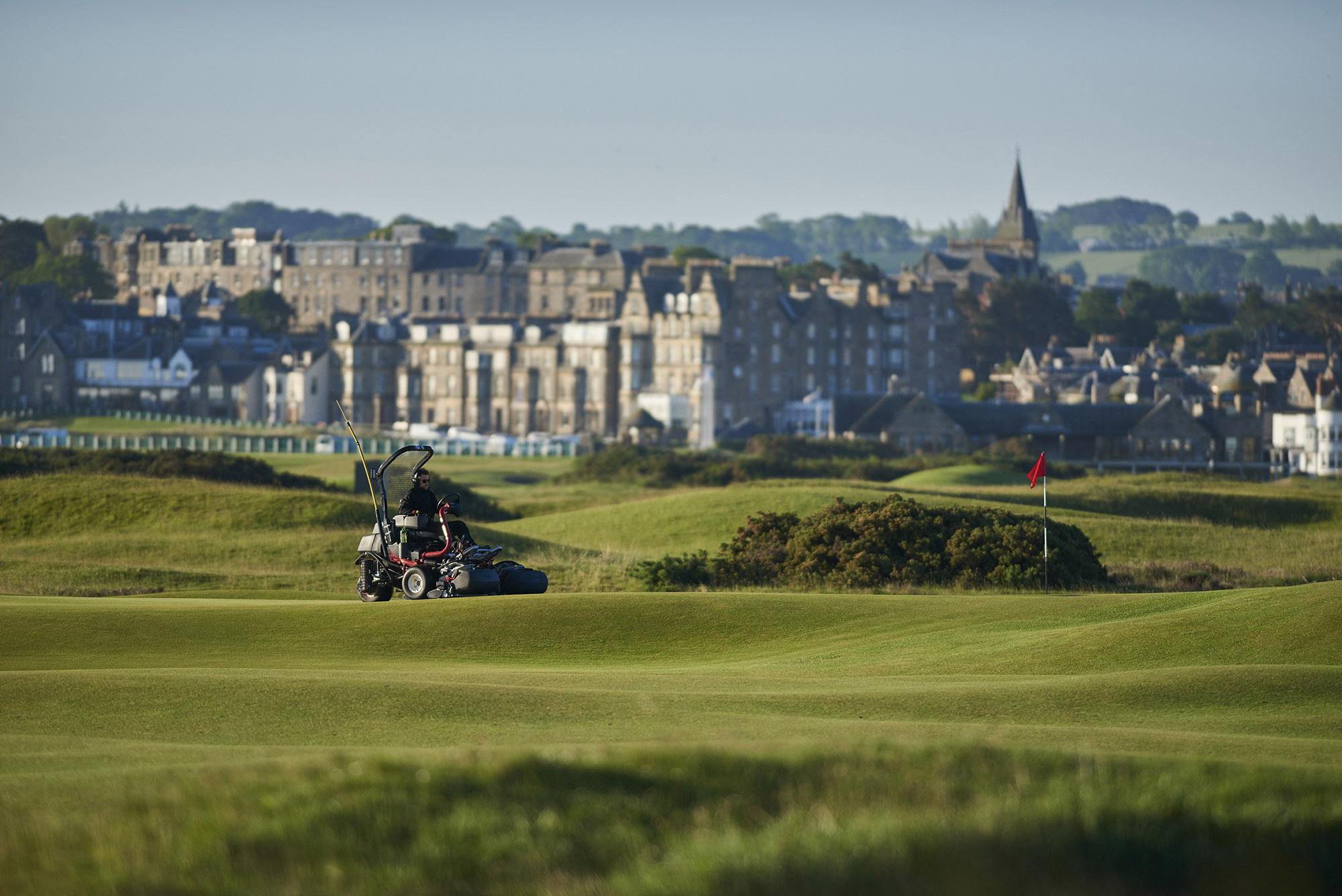 Toro mower on the greens at St Andrews Links with buildings in the background