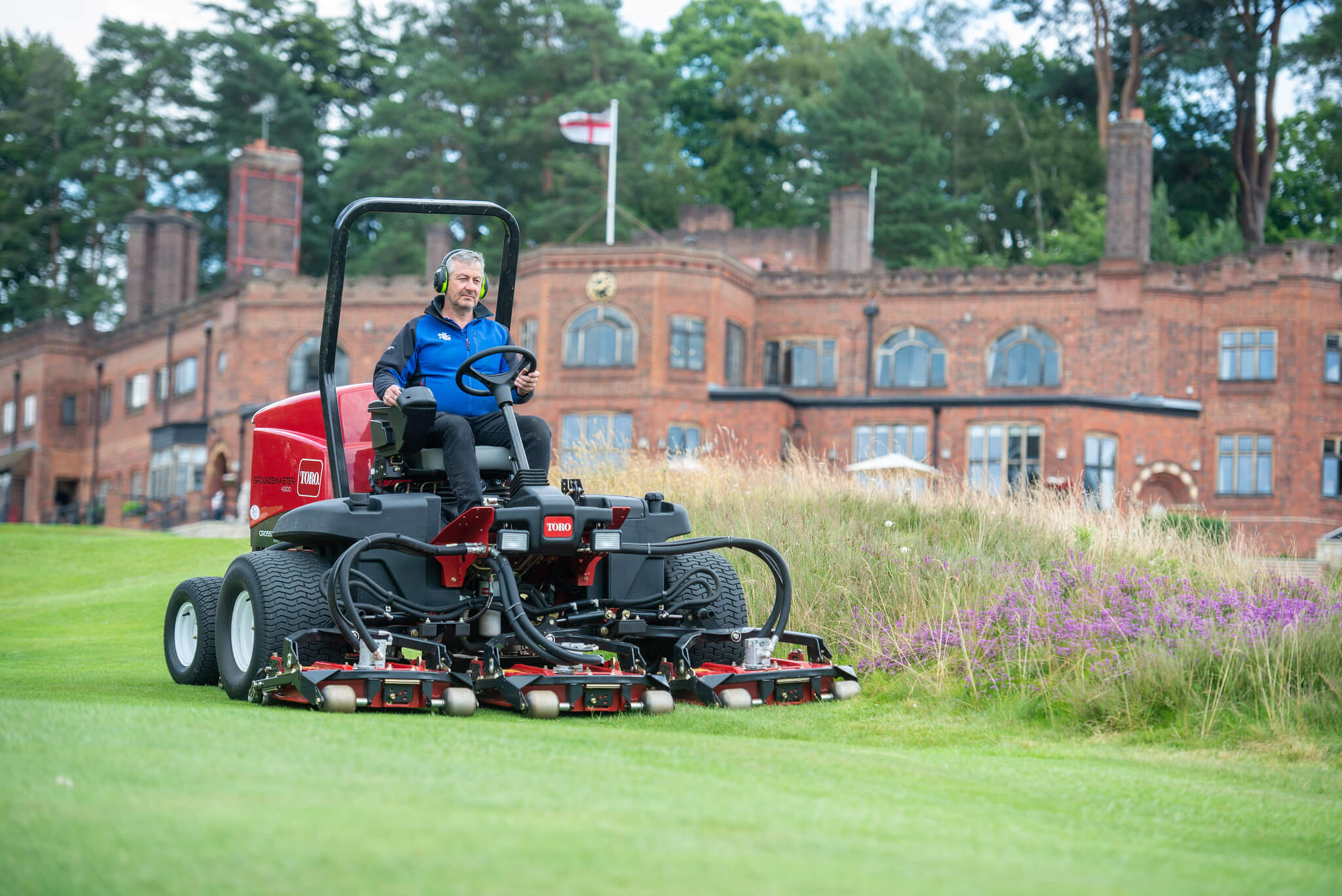 Toro mower on the greens at St George’s Hill with estate home in the background