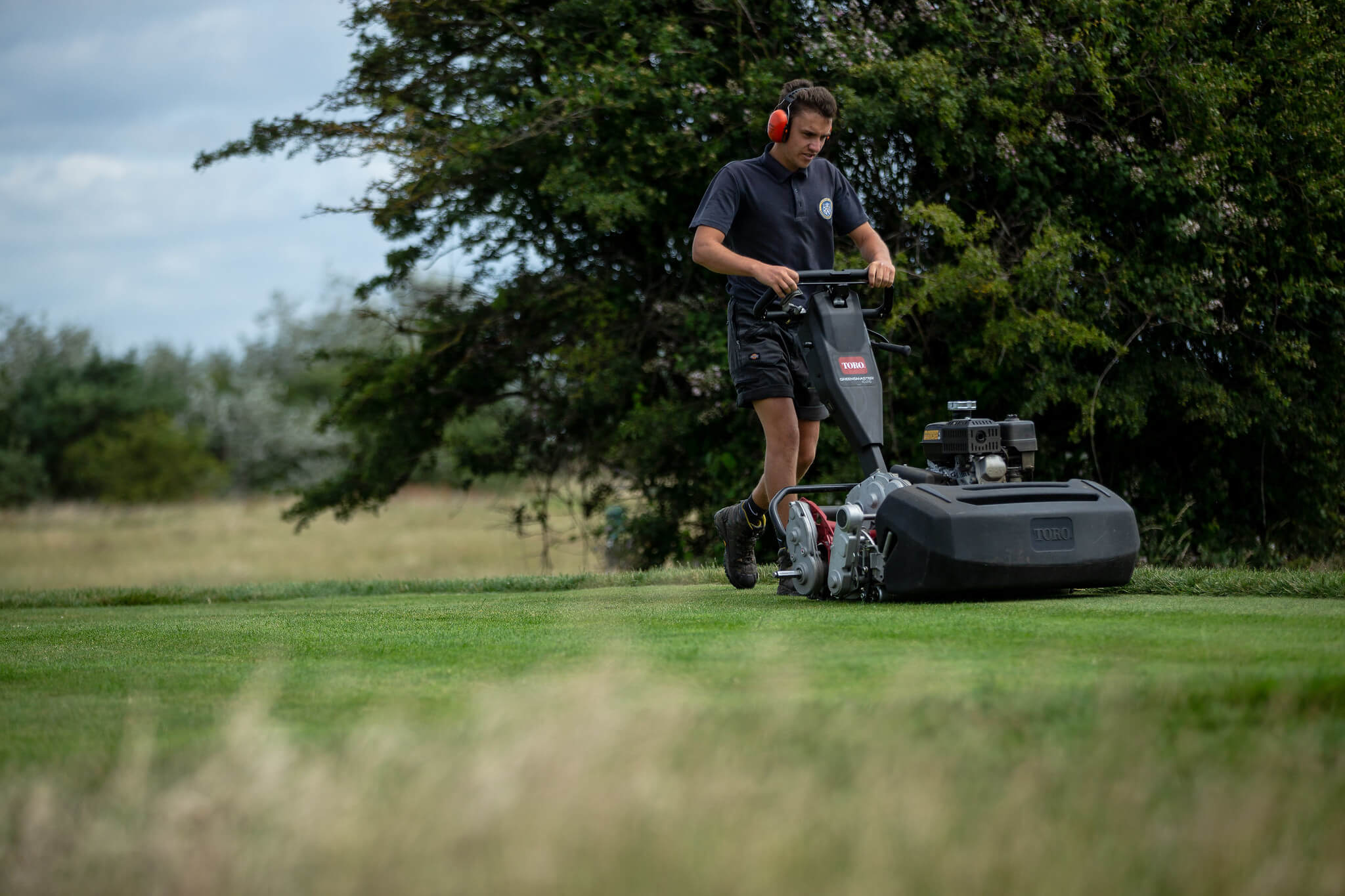Greenkeeper using a Toro walk-behind mower on the greens at Sheerness Golf Club