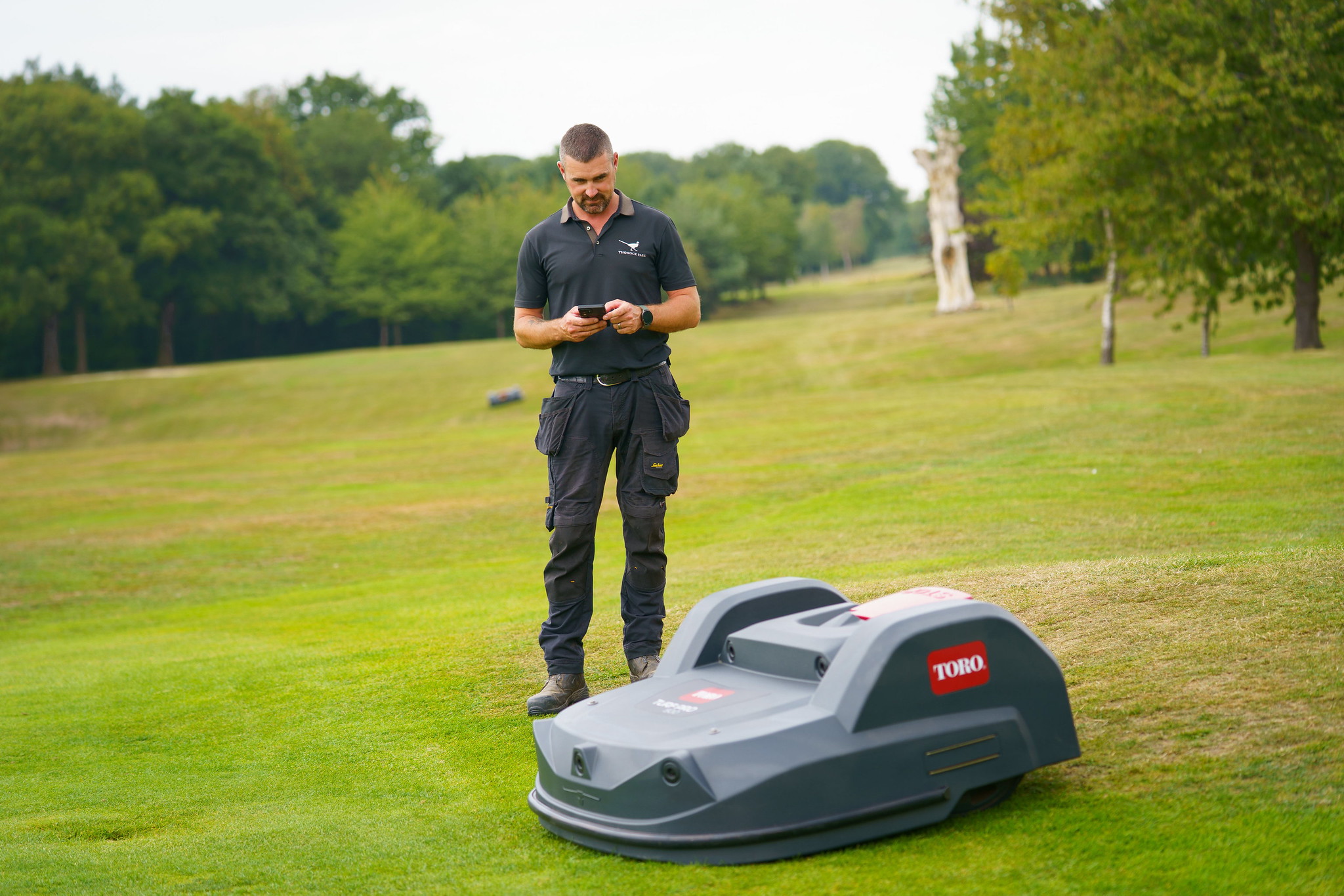 Thonock park course manager using his mobile phone while a Toro Turf Pro autonomous mowers mows in the foreground