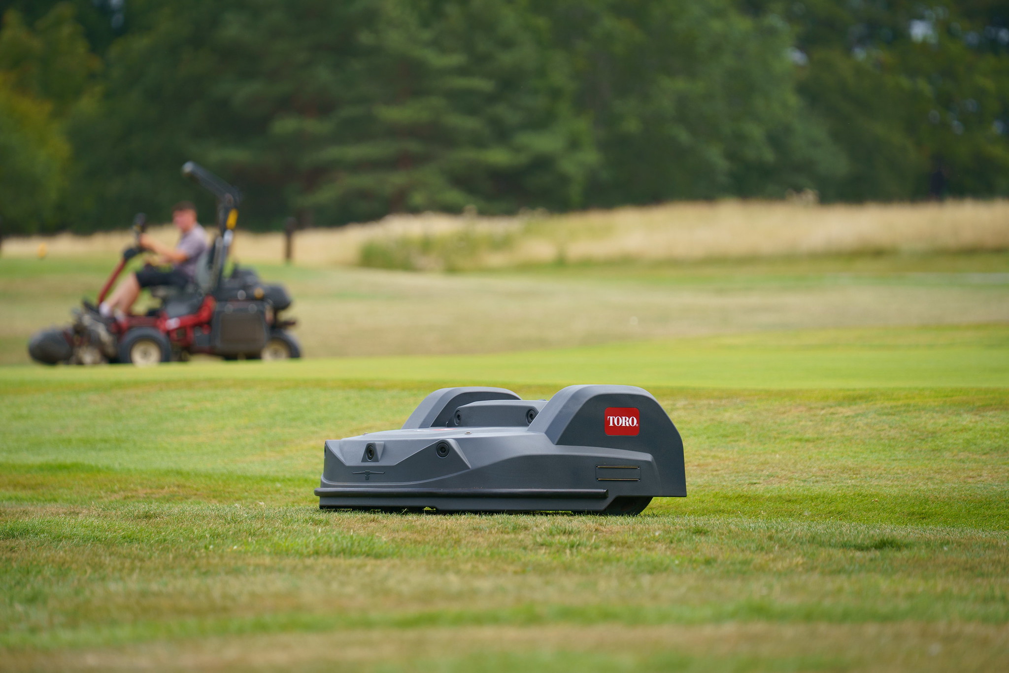 A Toro Turf Pro mower is mowing a golf course while a Toro ride-on mower is operating in the distance