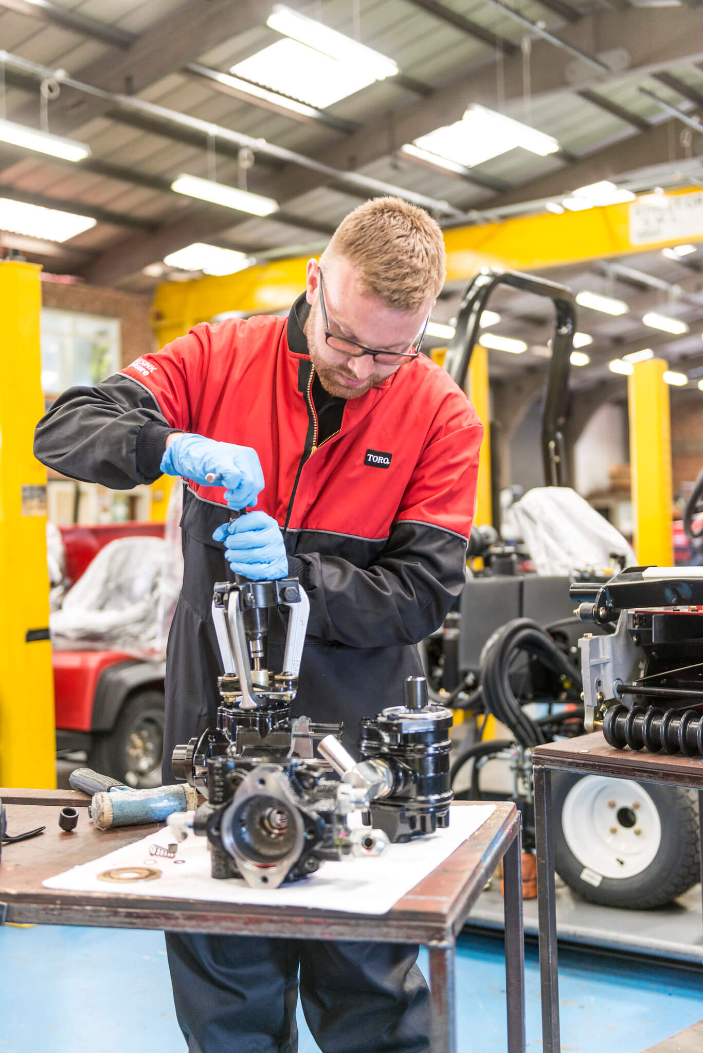 Turfcare mechanic stands working on a turfcare machinery part.