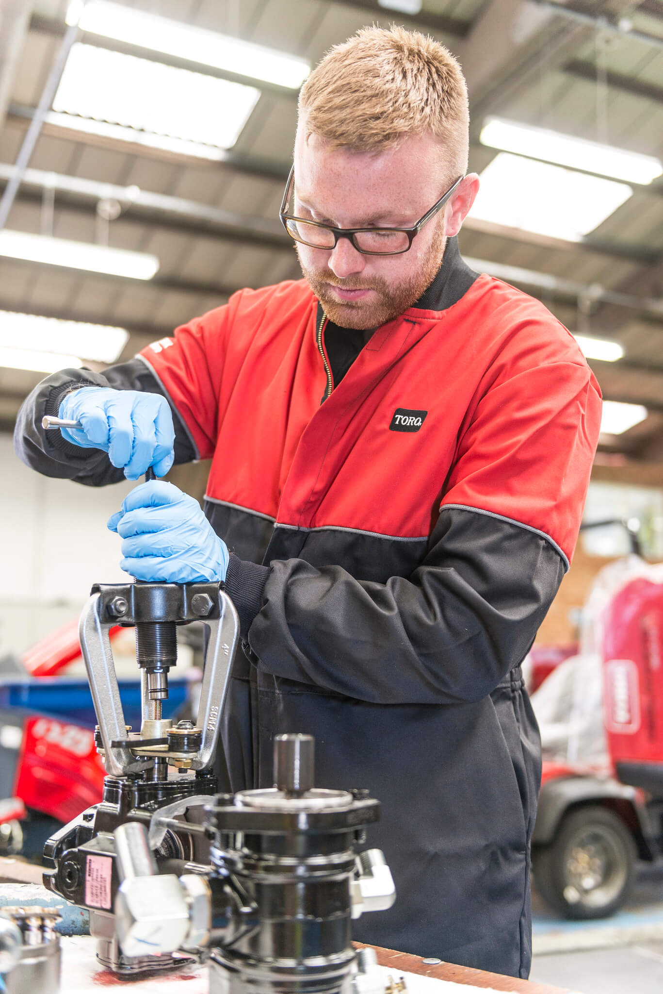Turfcare mechanic stands working on a turfcare machinery part.