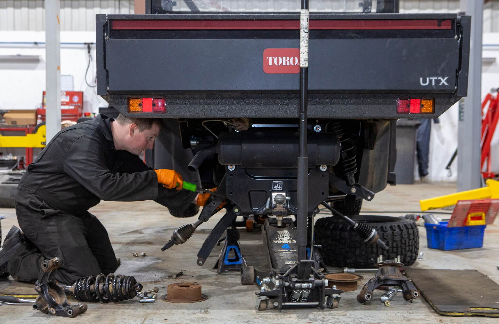 Turfcare mechanic kneels down underneath a raised Toro Workman utility vehicle to fix it.