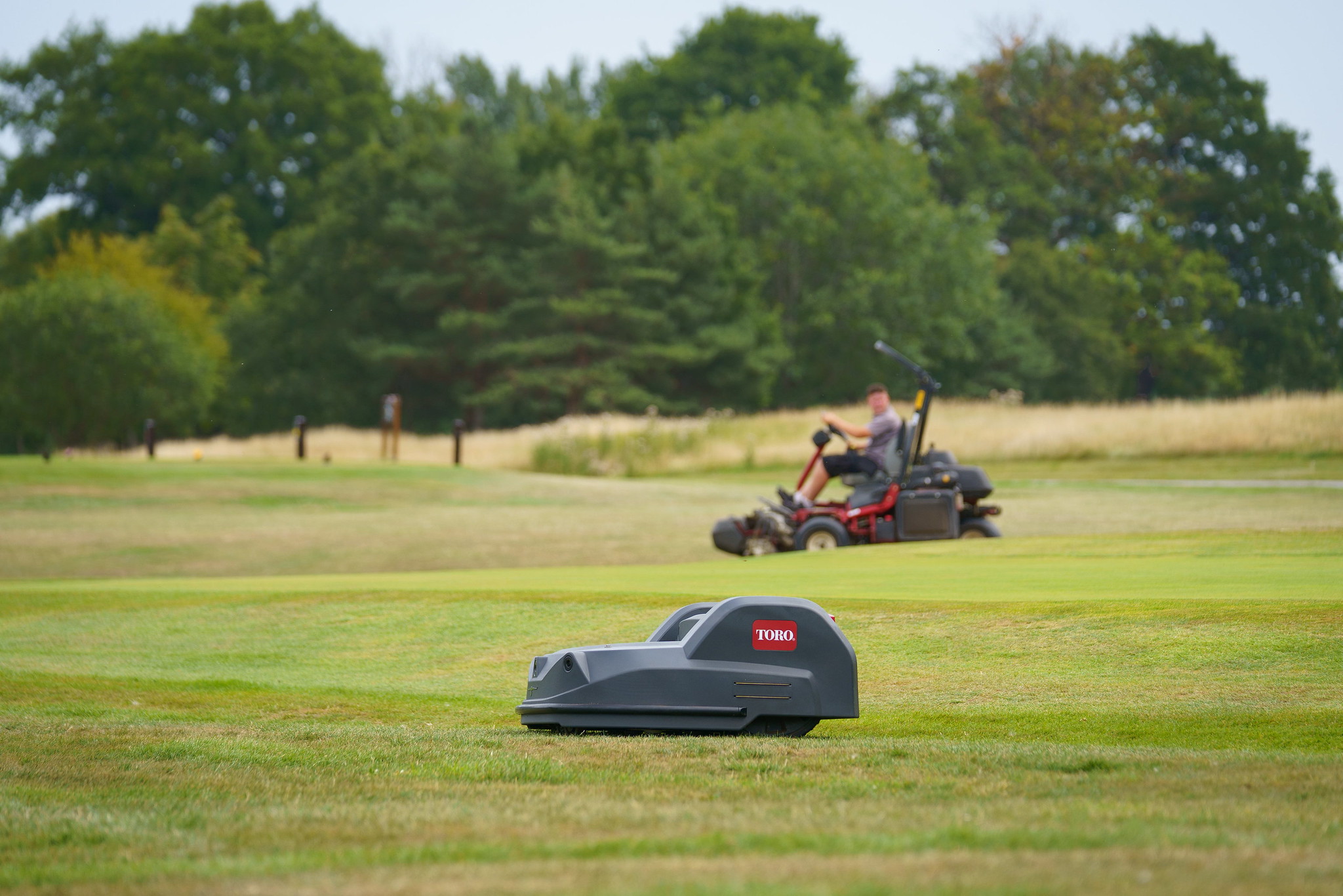 A Toro Turf Pro mower autonomously mows a golf course while in the background is a greenkeeper on a ride-on mower.