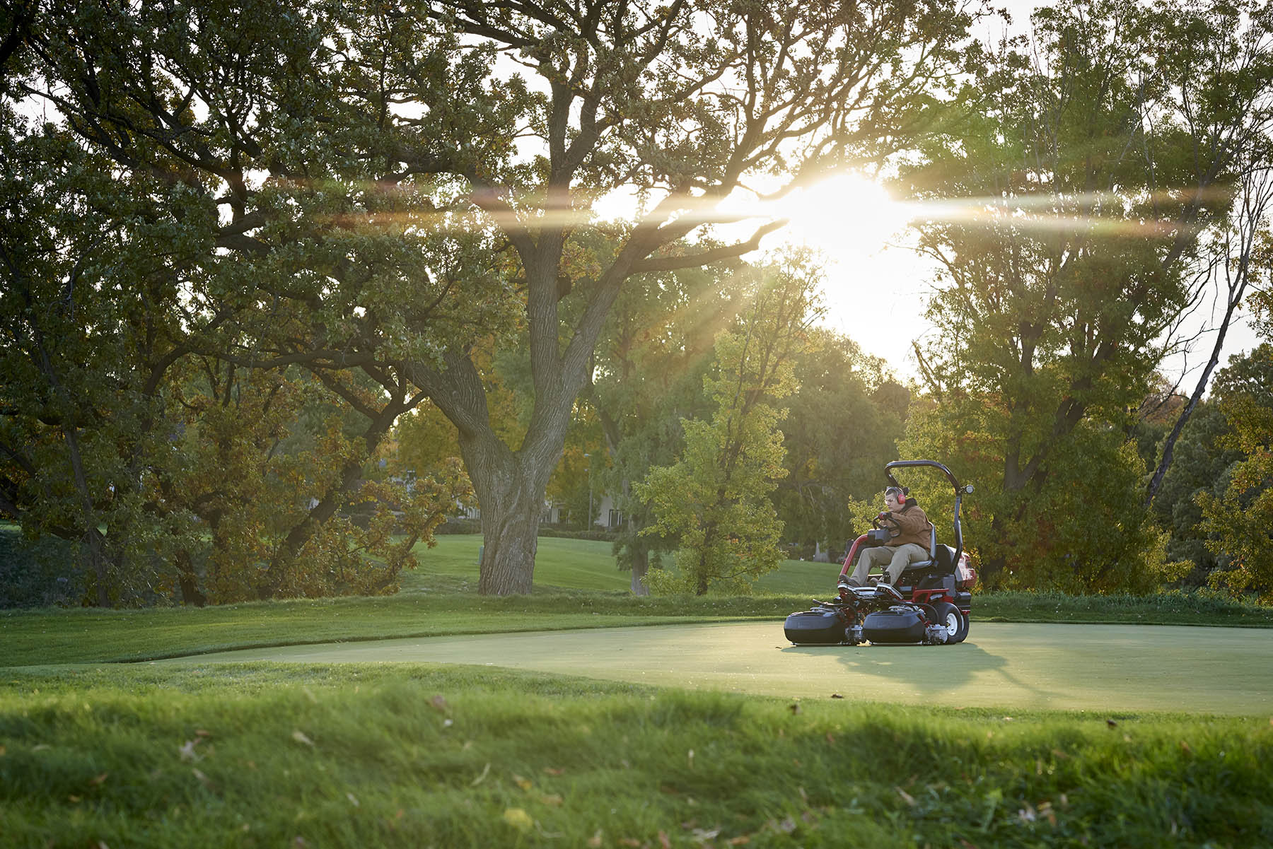 A greenkeeper rides on a Toro eTriFlex 3370 mowing a golf course green