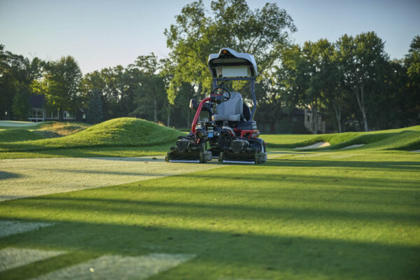 A Toro autonomous fairway mower self-mows a golf course with trees in the background.