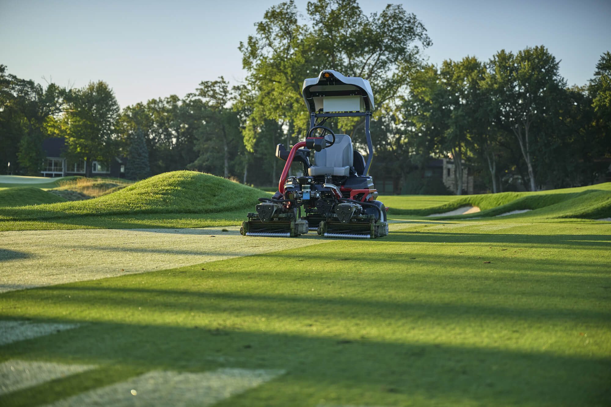 A Toro autonomous fairway mower self-mows a golf course with trees in the background.