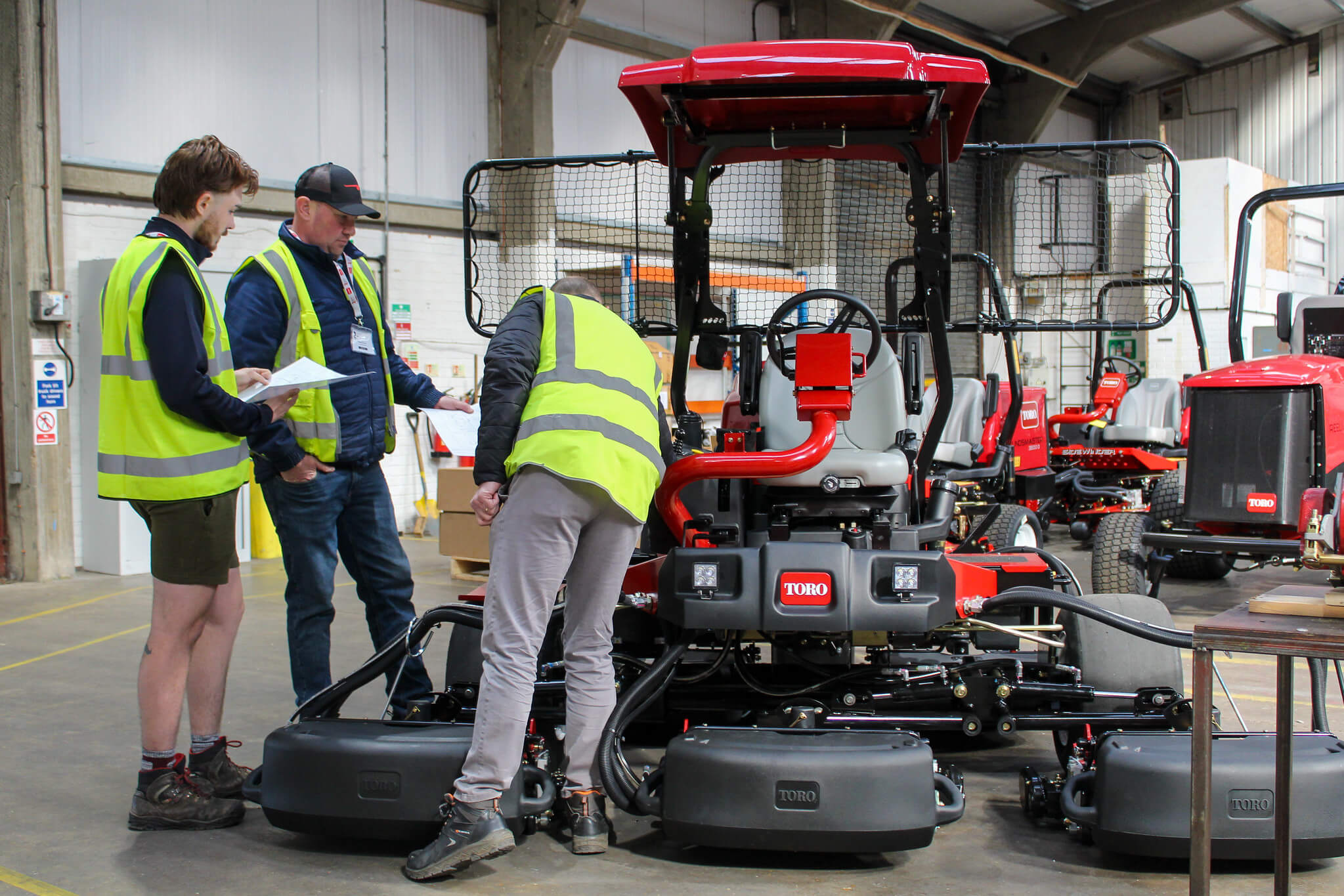 Three turf professionals in a workshop looking at a Toro mower.