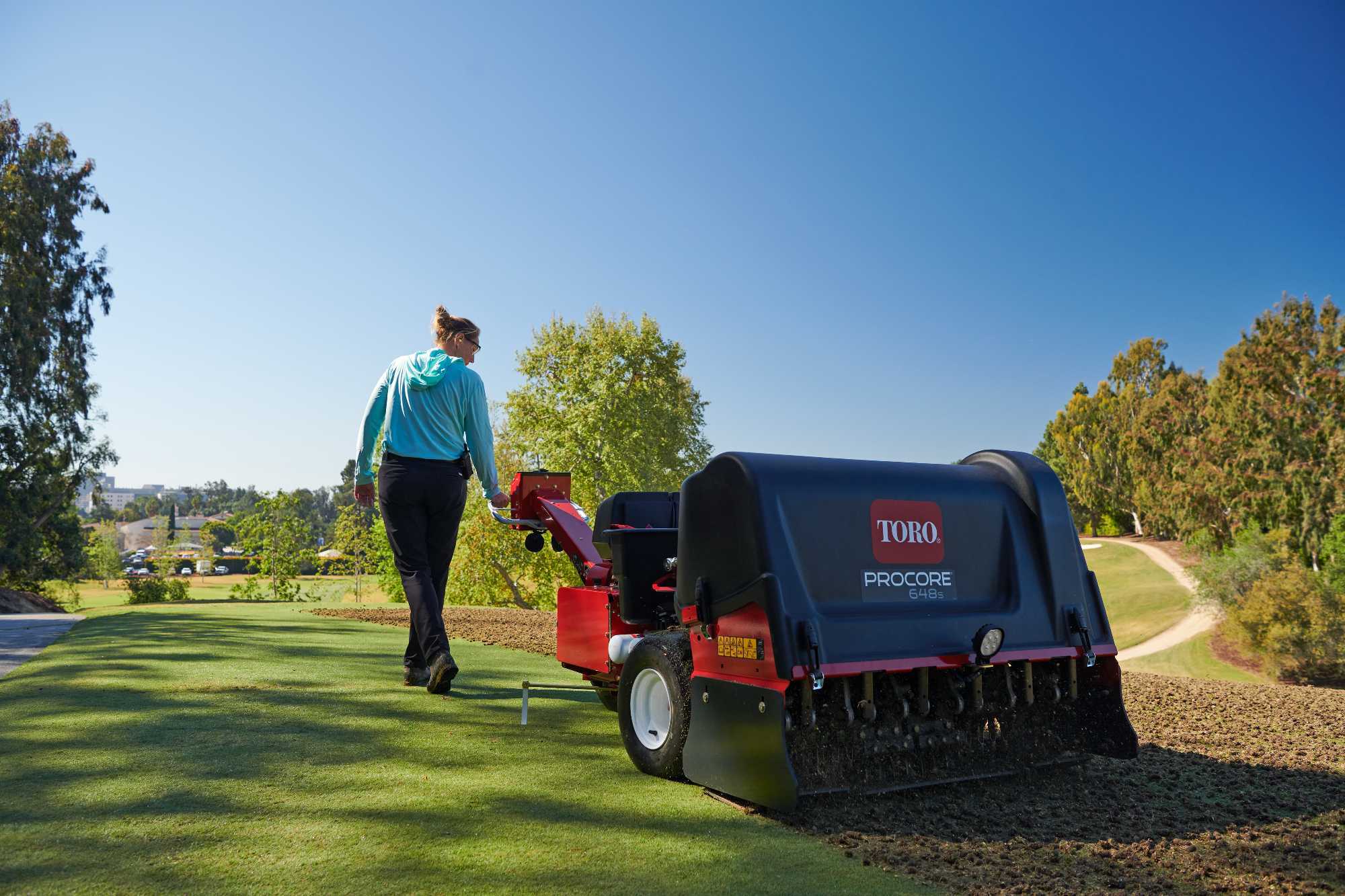 A greenkeeper pulls a Toro ProCore 648s aerator along a golf course.