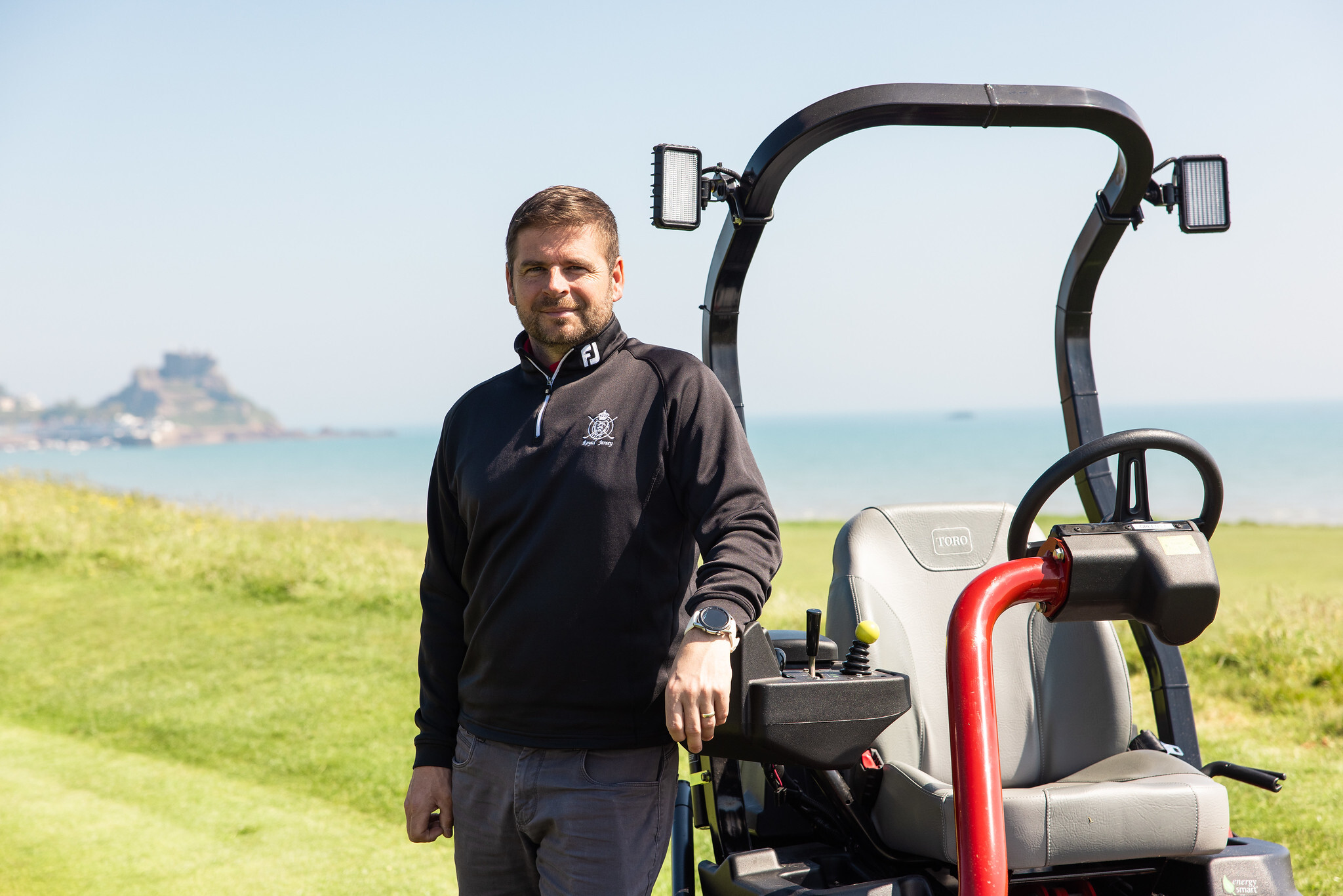 Allan Black, Course Manager at Royal Jersey Golf Club standing next to a Toro mower on the golf course.