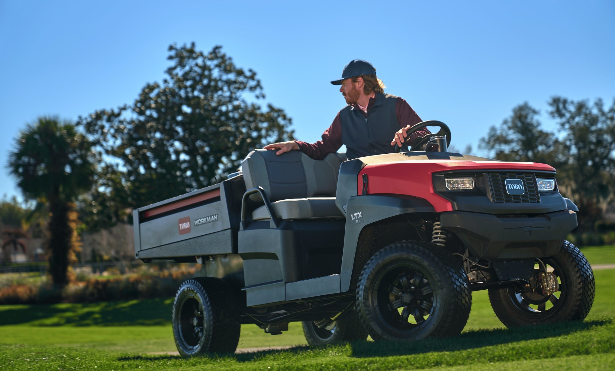 A greenkeeper driving a Toro Workman LTX across a golf course.