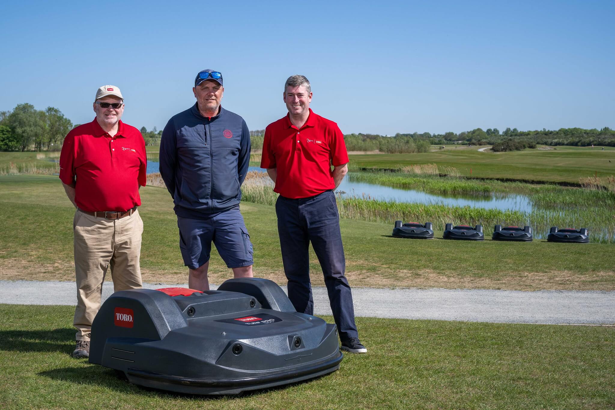 St Ives Golf Club course manager and two Reesink reps stand behind a Toro Turf Pro 500 mower on the course with four more autonomous mowers in the background.