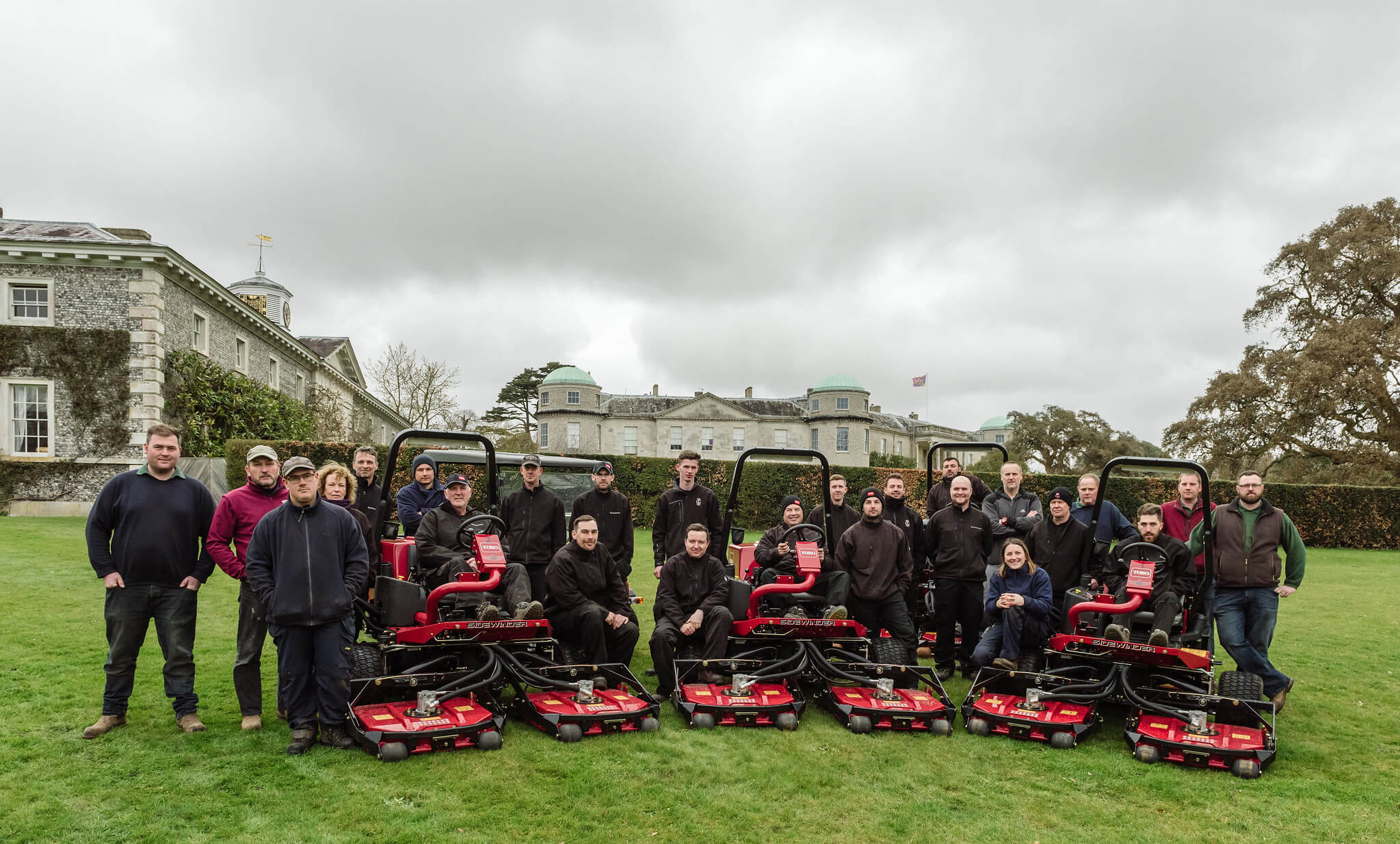 A fleet of Toro grounds machinery with a team of groundskeepers in front of the Goodwood estate building.