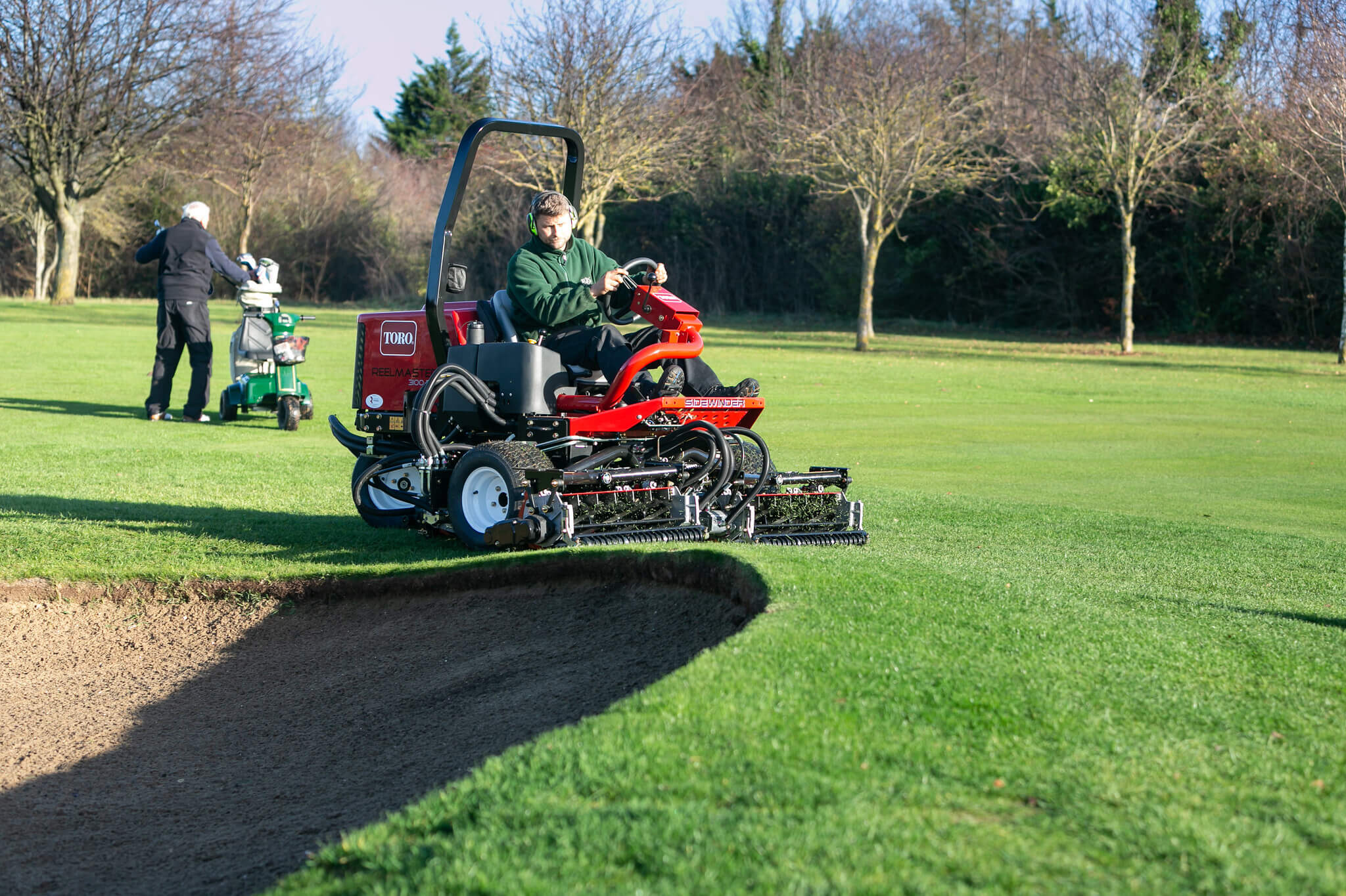 A Toro greensmower mowing around a golf course bunker.