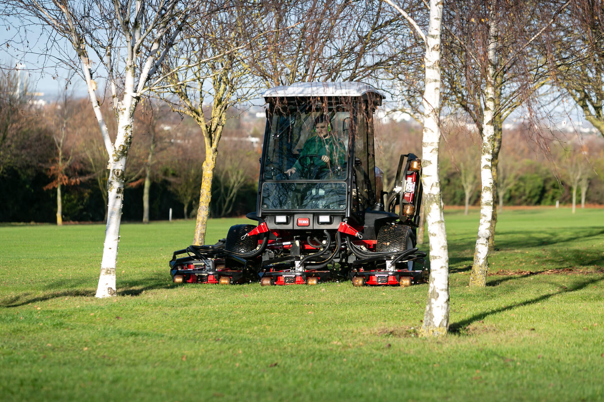 A Toro groundsmower with cab mowing between trees.