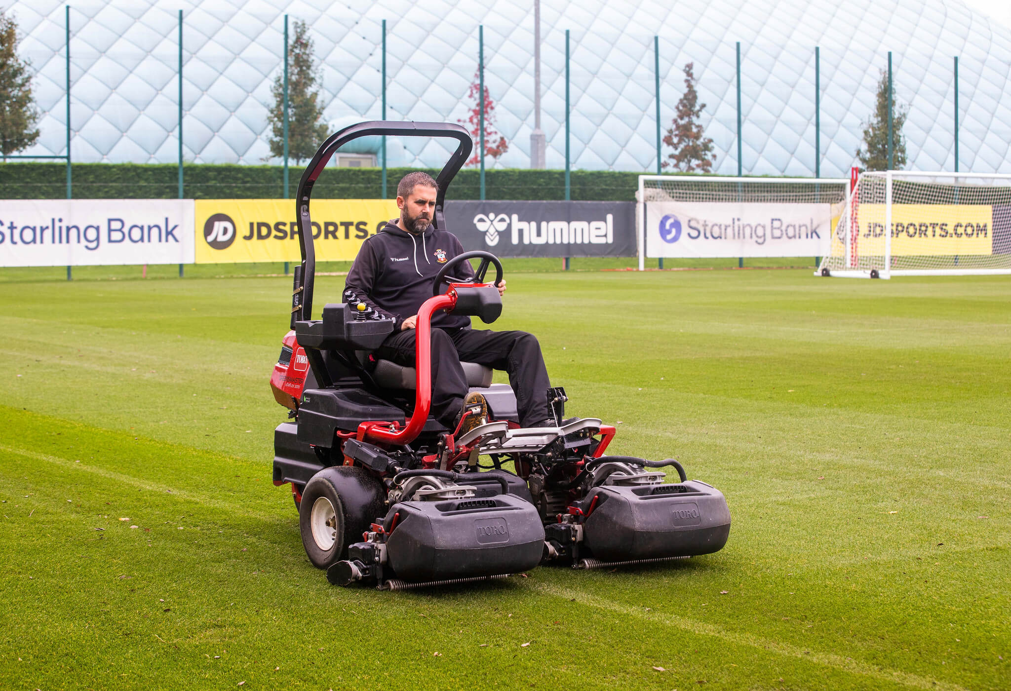 A groundsman mowing a sports pitch with a Toro ride on mower.
