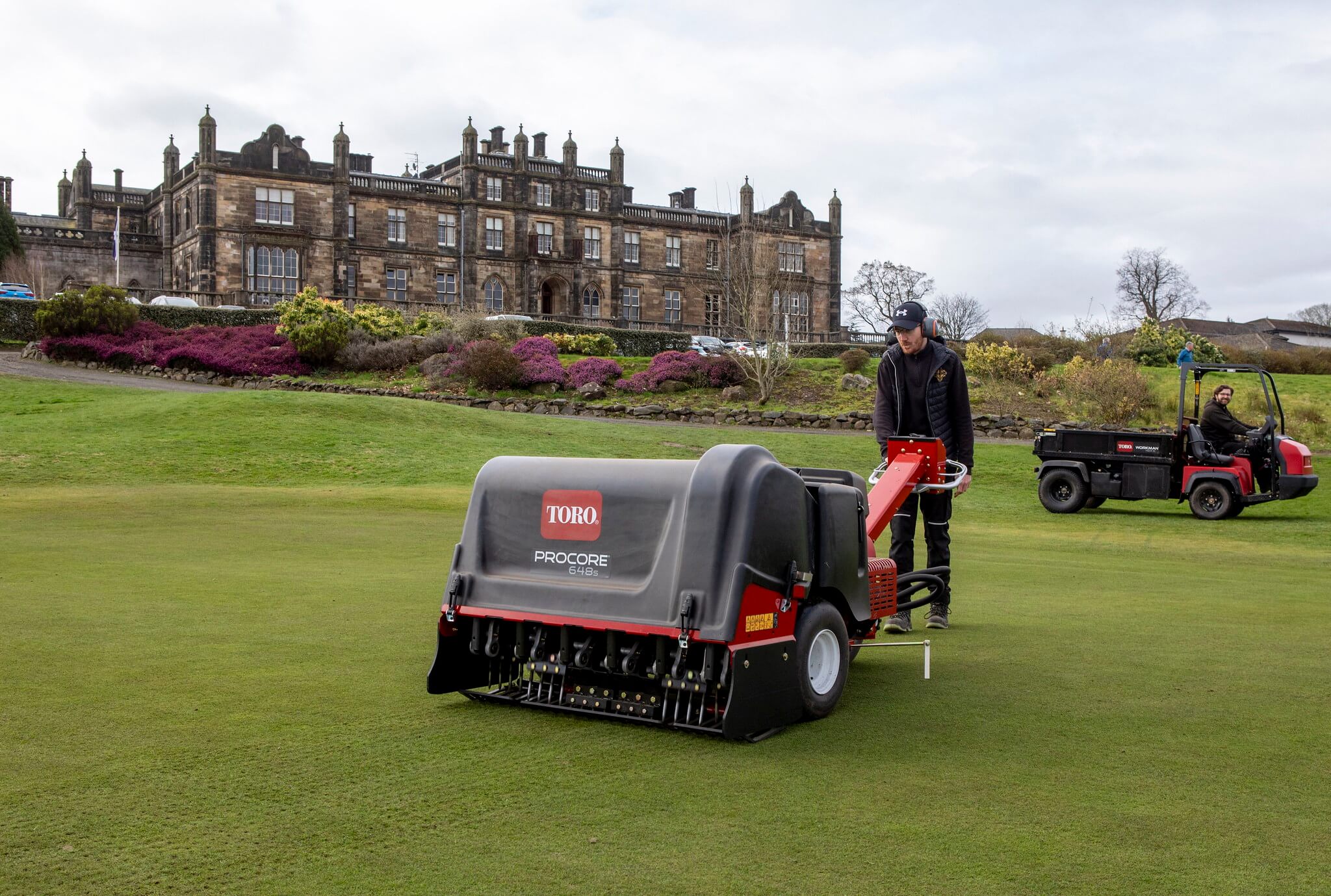 A greenkeeper using a Toro ProCore 648s aerator on a golf course.