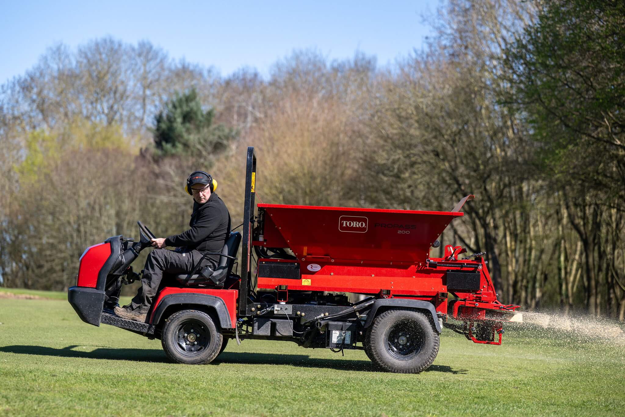 A greenkeeper operates a Toro topdresser on a golf course.