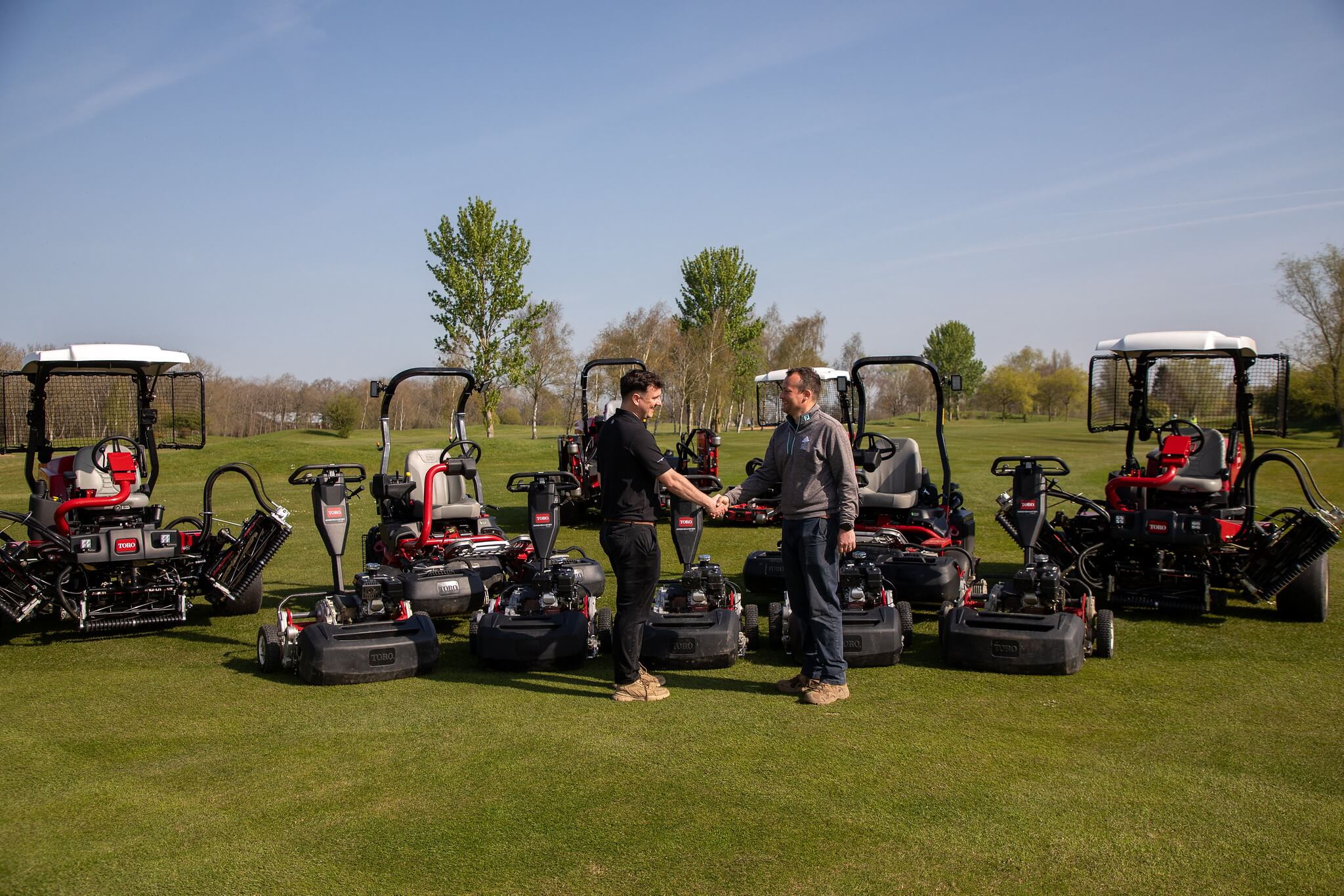 A Reesink rep and a golf course manager shake hands in front of a fleet of Toro machinery.
