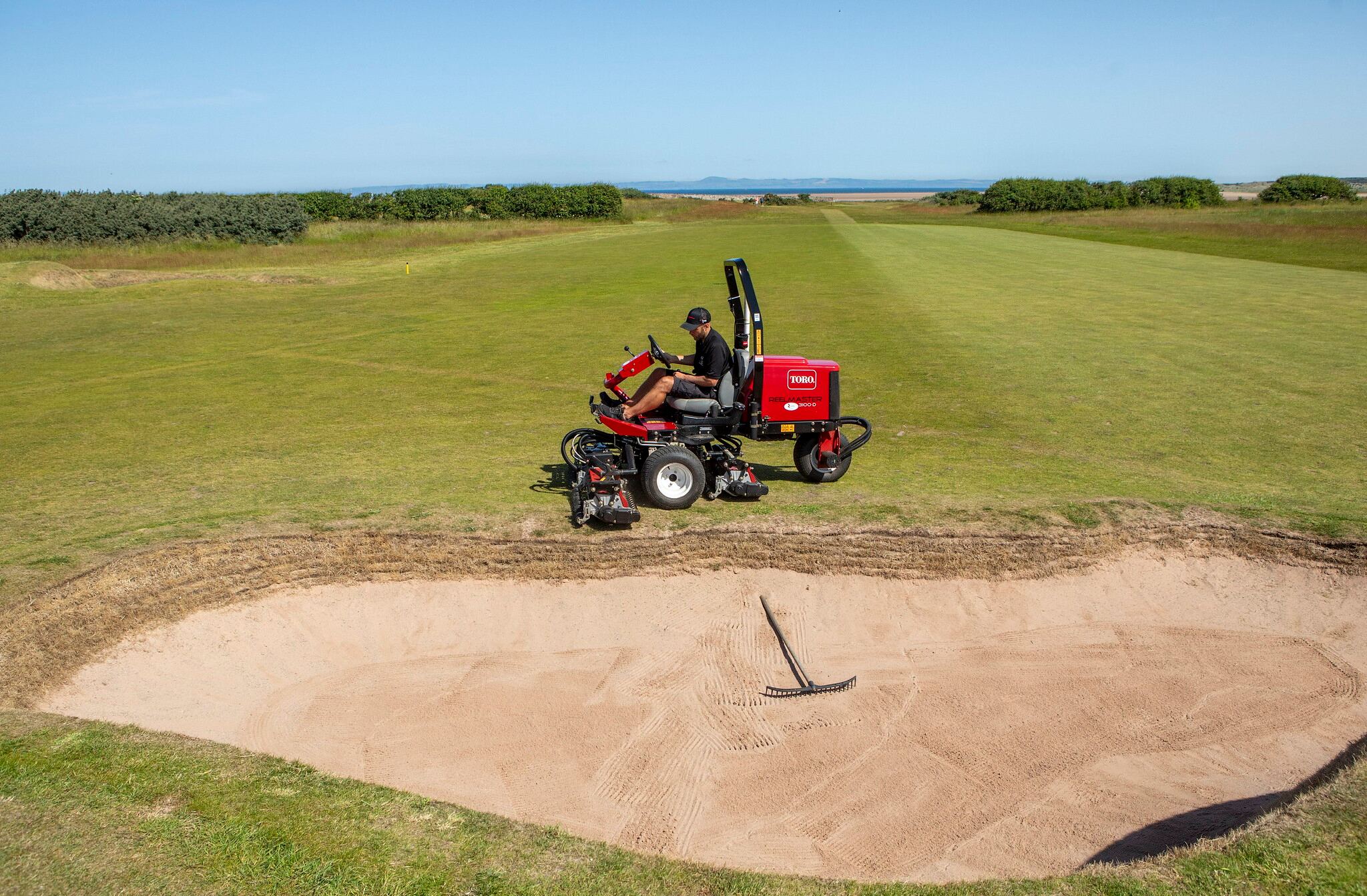greenkeeper sitting on Toro sidewinder mower on turf next to bunker
