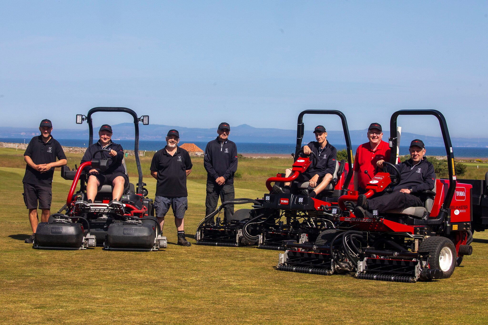 Craigielaw golf club greenkeeping team standing next to Toro mowers. Three members of the seven member team are sitting on the mowers.