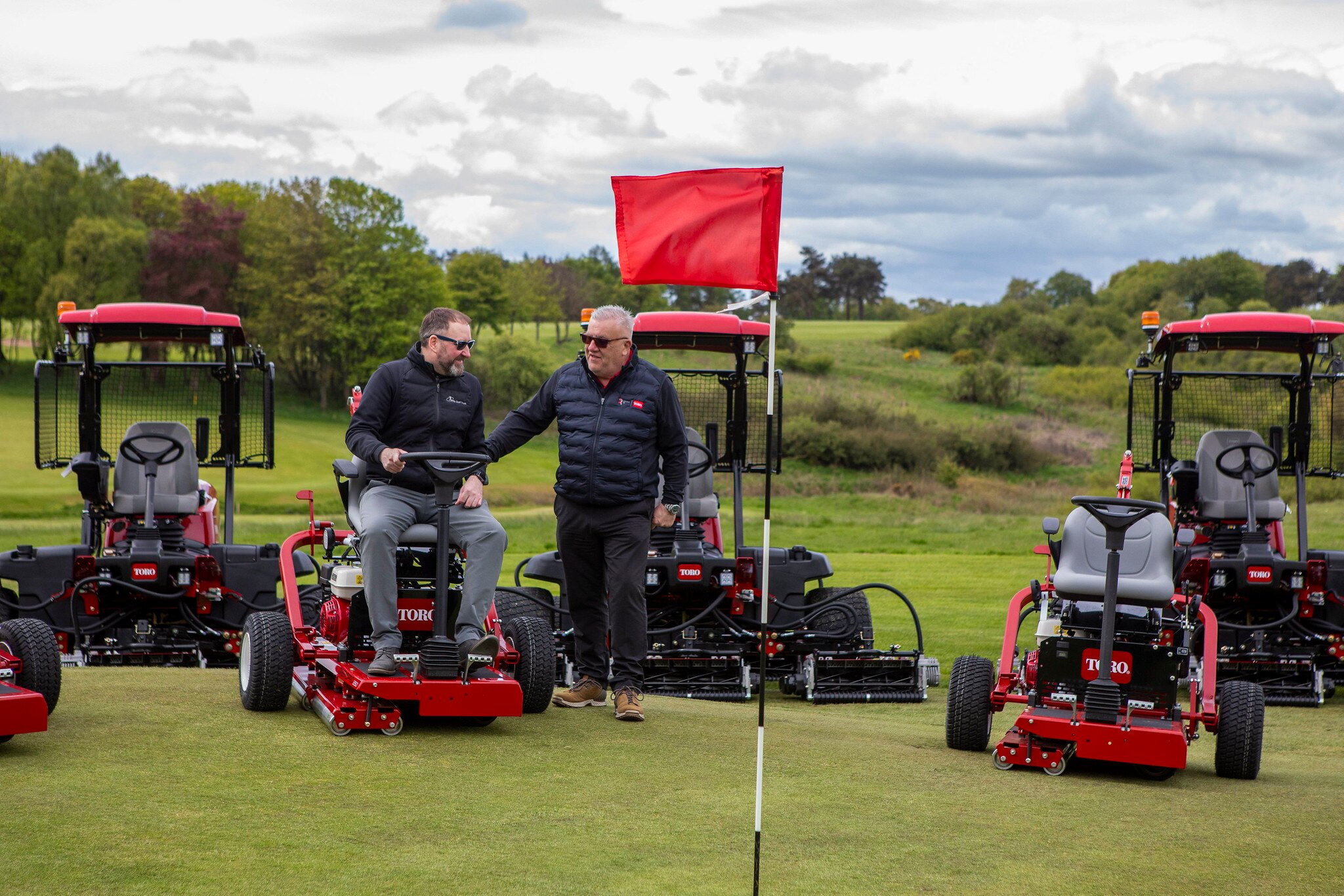 Fife golf trust's manager sitting on a Toro mower with Reesink sales rep talking beside the mower. They are surrounded by multiple other Toro machinery
