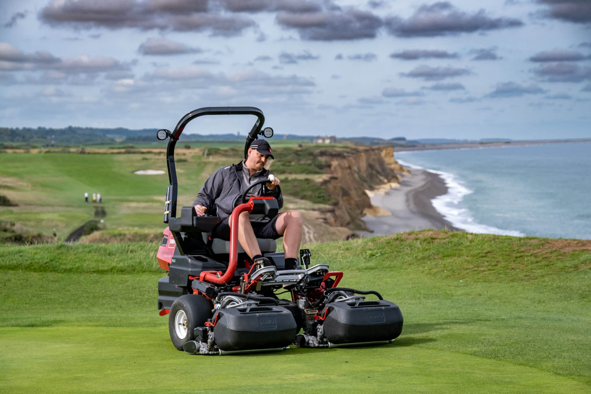 A Toro Greensmaster eTriFlex 3370 all-electric ride-on cylinder mower being used next to a cliff at Sheringham Golf Club.