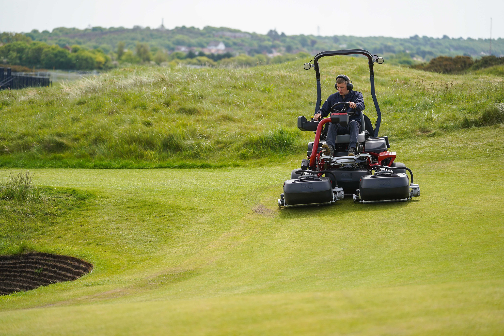 A greenkeeper mowing a golf course using a Toro Greensmaster eTriFlex 3370 all-electric ride-on cylinder mower.