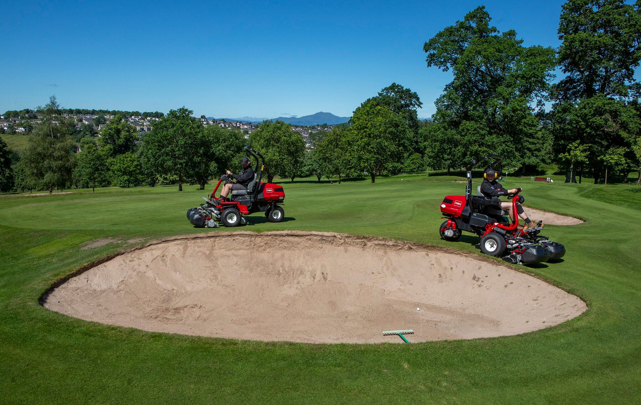 two red Toro ride-on mowers on Dunblane golf course near bunker.