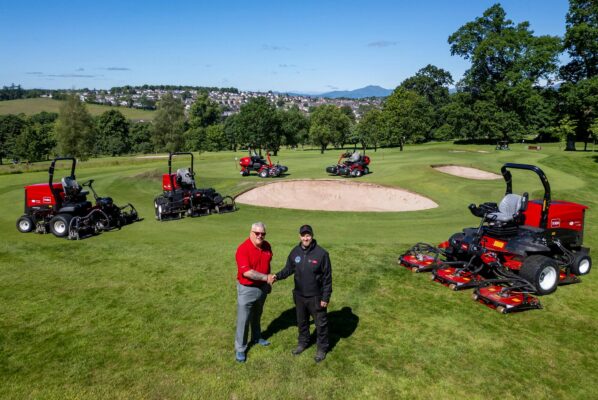 Reesink sales rep left shaking hands with Dunblane course manager right standing on golf course. There are five red Toro ride-on mowers in the background surrounding them.