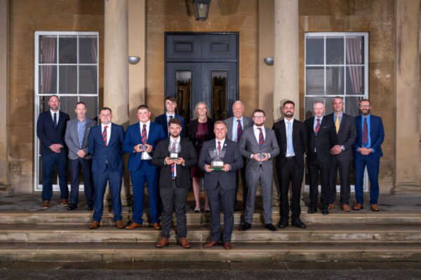 student award winners and runners up standing holding their awards. The award judges are stood behind all the winners with a building behind them