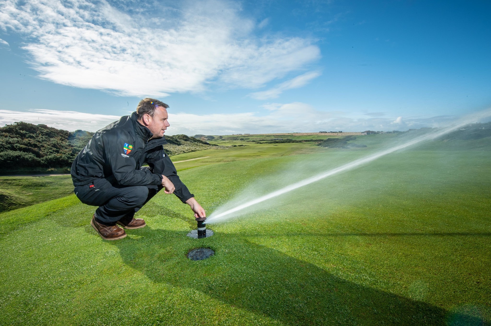 A Cruden Bay Golf Club greenkeeper adjusts the positioning of a Toro Irrigation sprinkler in the turf.